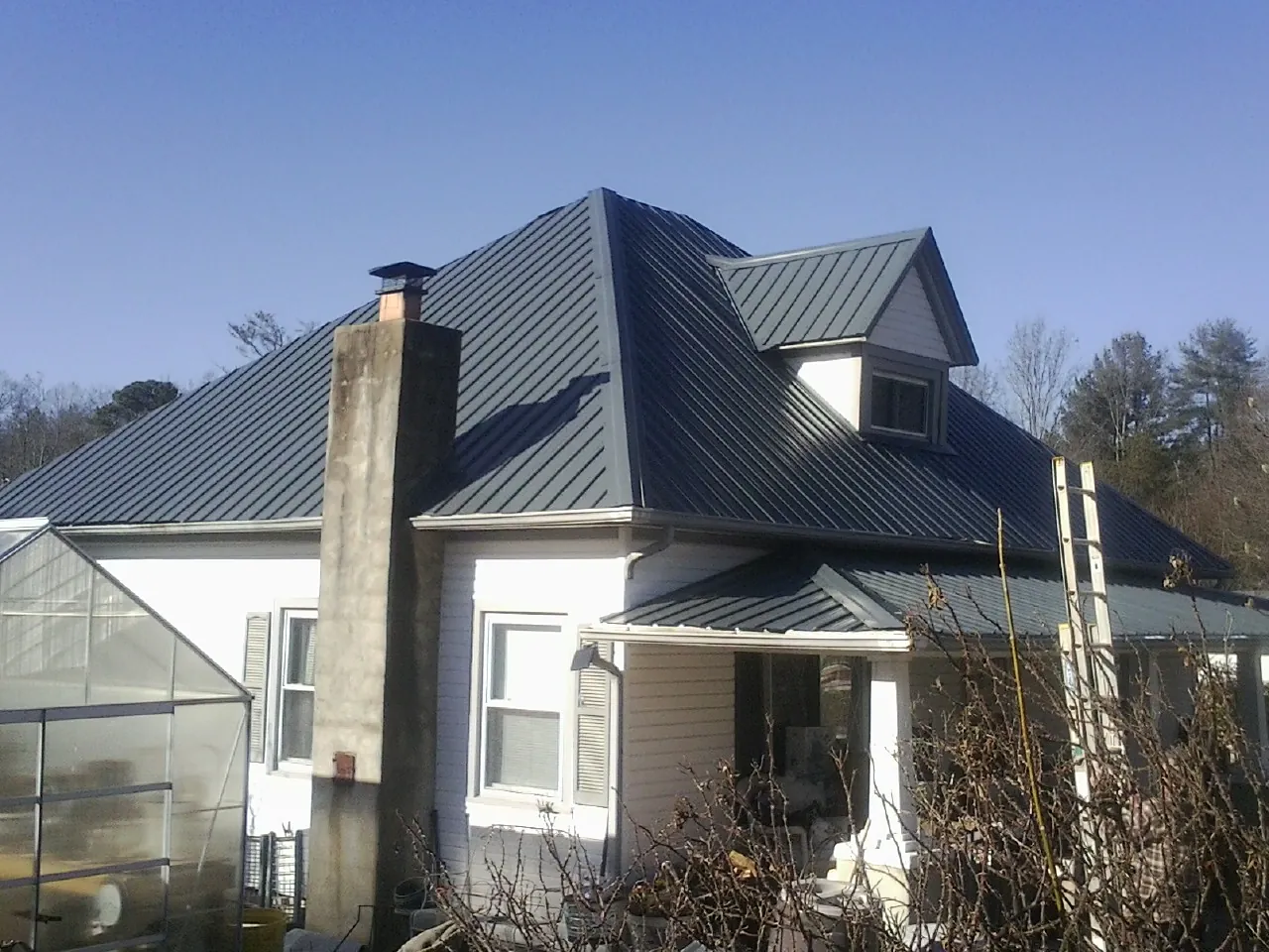 Dark blue standing seam metal roof on a white farmhouse with dormer — Slate & Tile Roof Repair by Roofing Brothers in Firestone