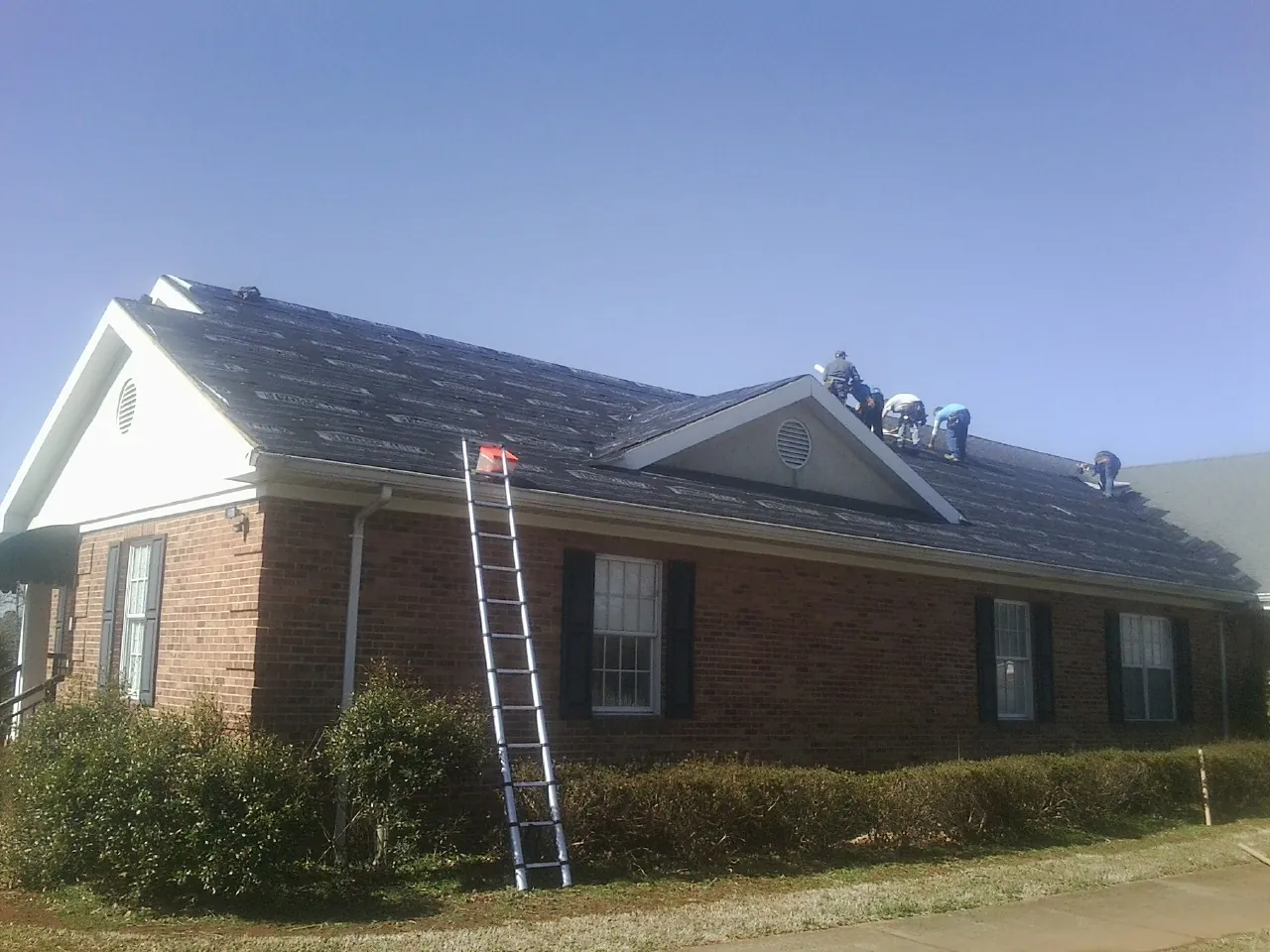 Crew tearing shingles off a brick ranch roof with a ladder set — Emergency Roof Repair work by our crew in Firestone