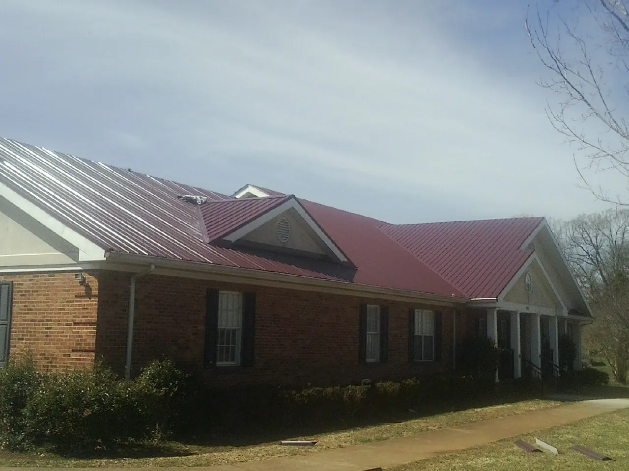 Red metal roof with gabled entries on a long brick building, from a Hail Damage Roof Repair job in Firestone