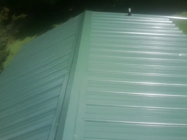 New green metal panels meeting at the ridge of a roof — Flat Roof Repair work by our crew in Firestone