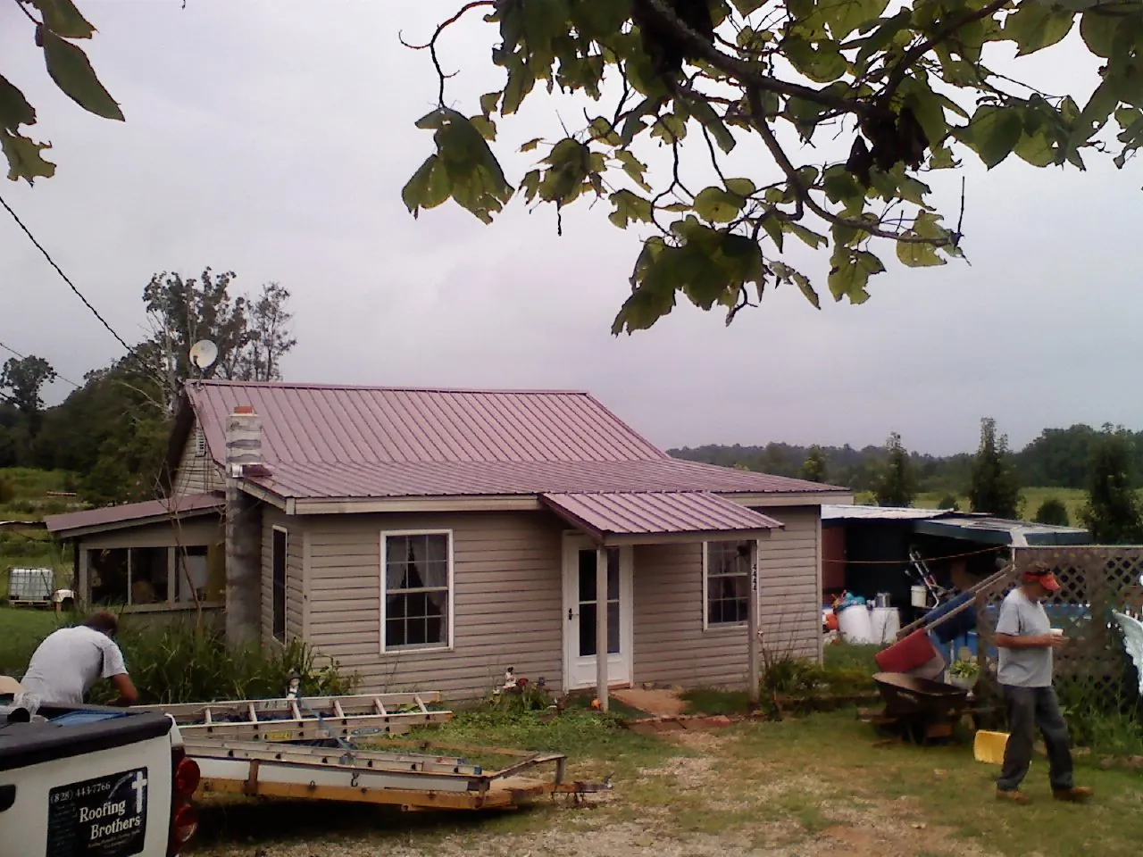 Crew finishing a mauve metal roof on a small farmhouse in Firestone
