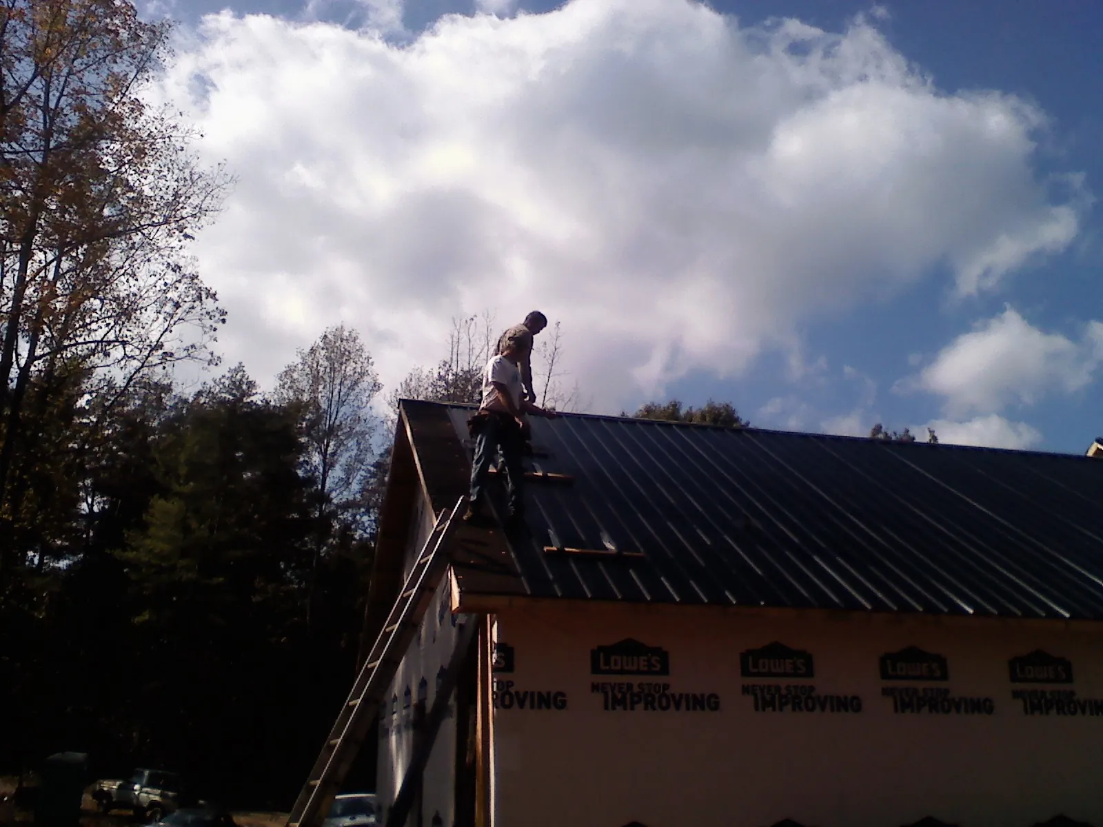 Roofer fastening dark metal panels high against a cloudy sky, from a Roof Inspection job in Firestone