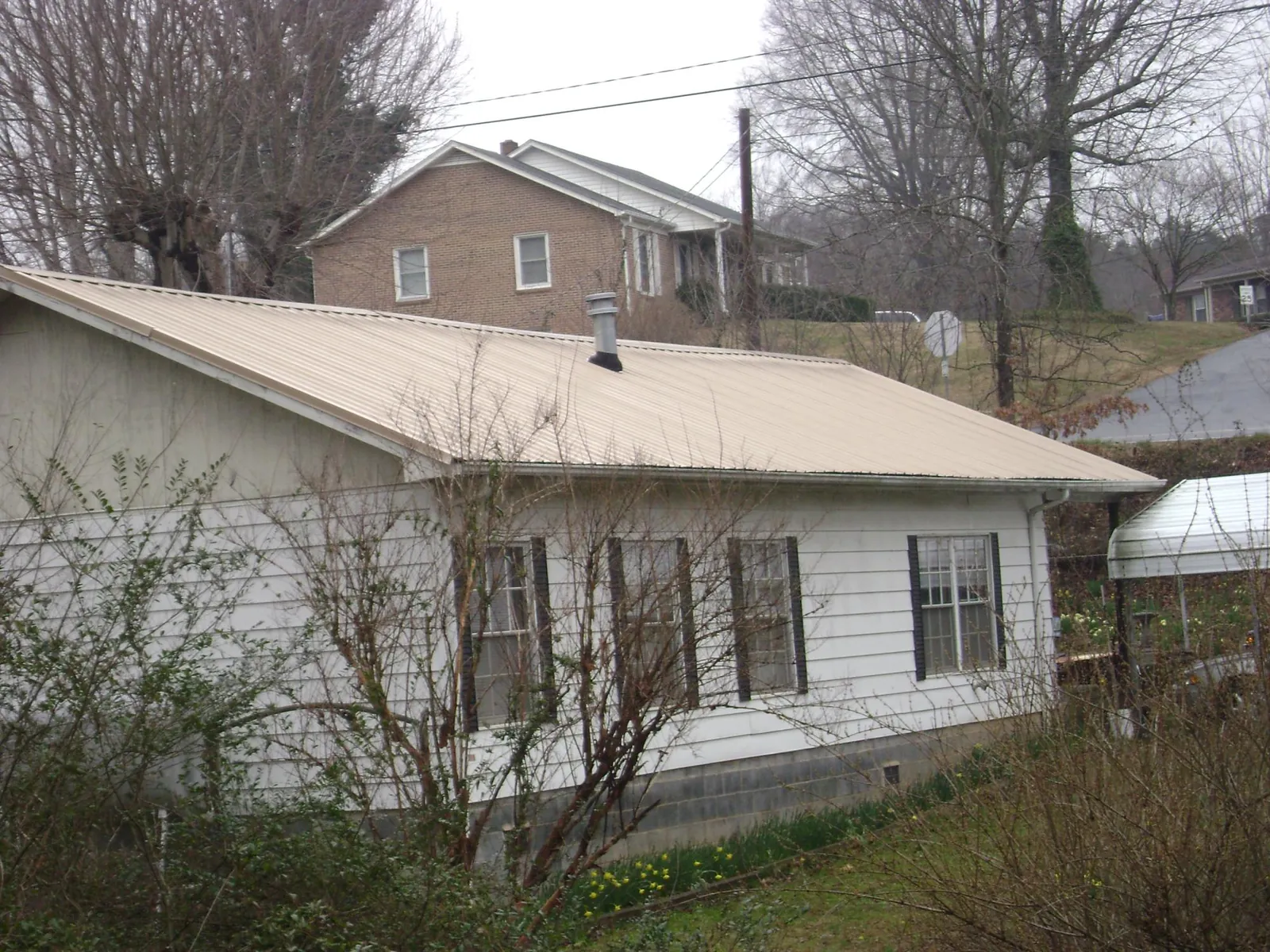 Tan metal roof on a white sided house set into a hillside — Commercial Roofing by Roofing Brothers in Firestone
