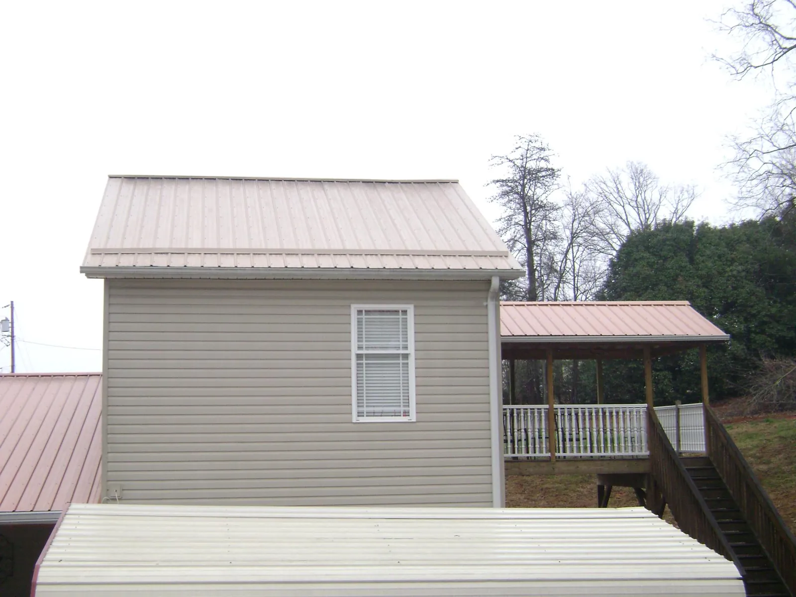 Tan metal roofs on a two story addition and attached porch, from a Roof Replacement job in Firestone